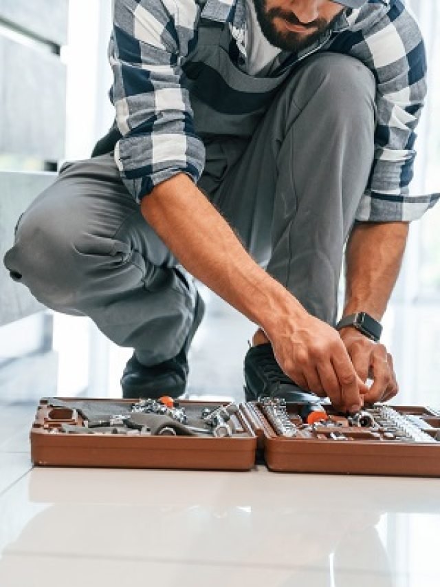Case with equipment. Plumber in uniform is indoors at home